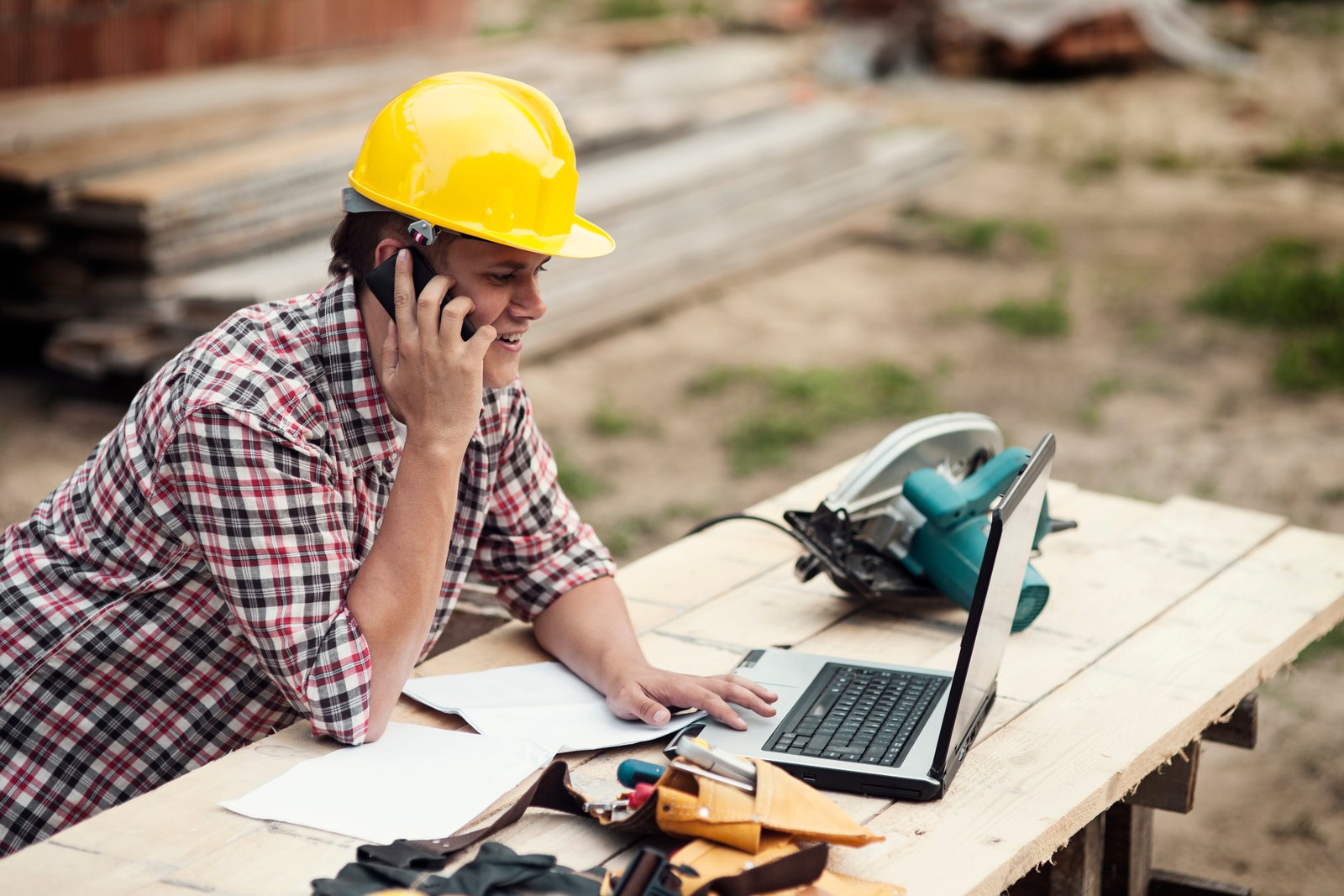 Homem com capacete usando celular e laptop em ambiente de mineração